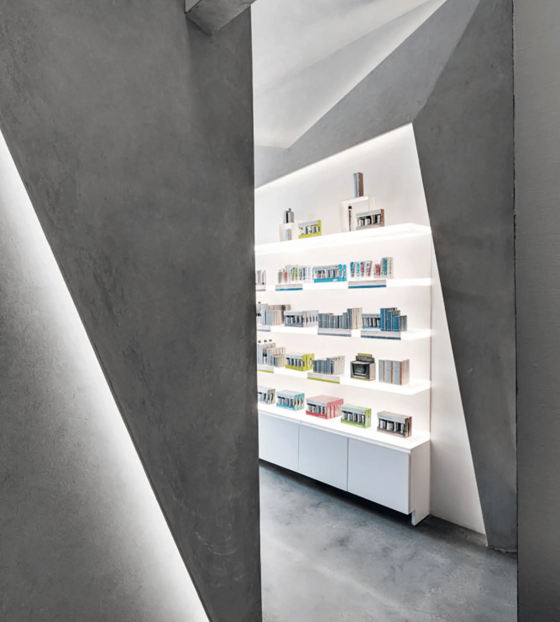Angular concrete walls opening onto a backlit shelf wall of skin care products.